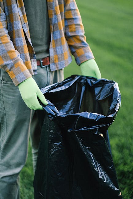 A small, dark red flatbed truck with a metal safety cage at the front and open cargo area at the back, loaded with various waste materials including large white bags and black plastic trash bags, park
